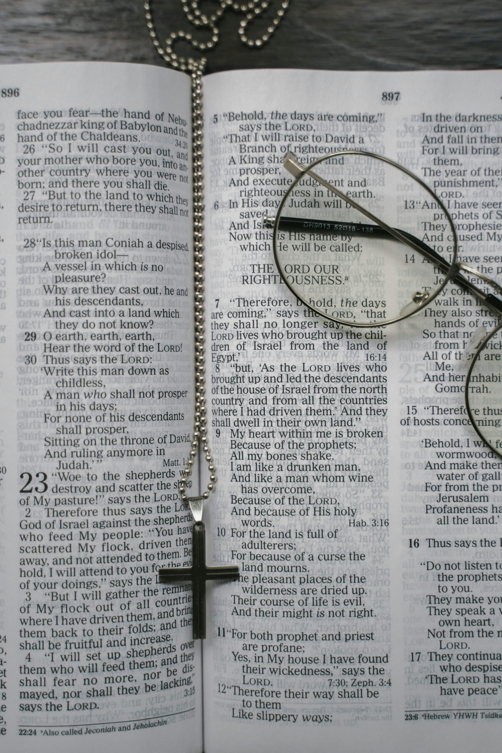 An open Bible with a cross necklace and glasses placed on the pages, symbolizing faith.